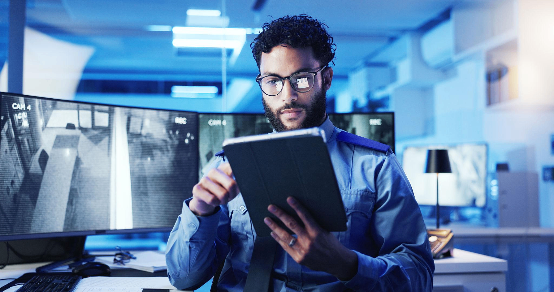 Security officer reviewing corporate surveillance feeds on a tablet inside a control room