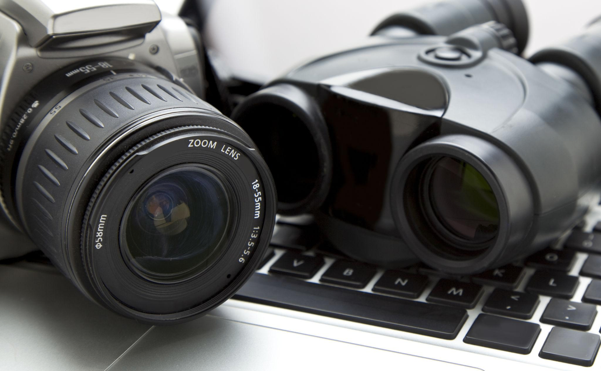 Surveillance camera and binoculars resting on a laptop — tools of discreet investigation work